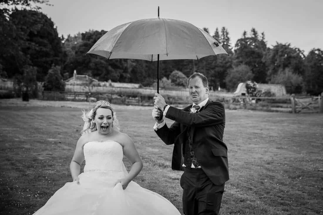 wedding couple running away from the rain holding umbrella